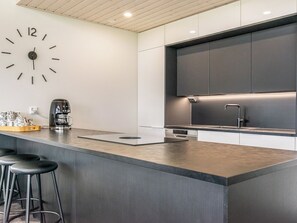 A modern kitchen with a large island, bar stools, a coffee machine, and a wall clock. - Villa hill magia by Interhome (Kuhmoinen)