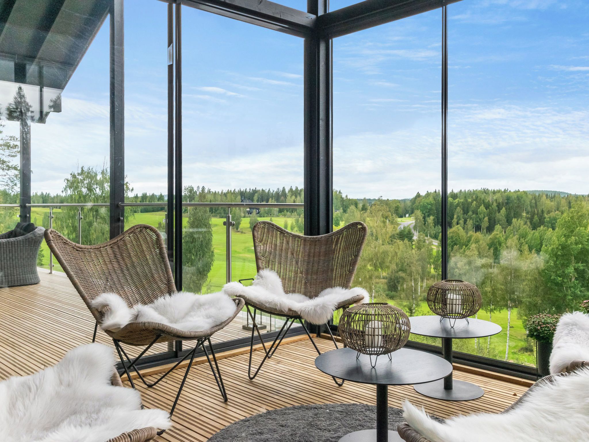 A modern outdoor seating area with wicker chairs and a round table, overlooking a lush green landscape.