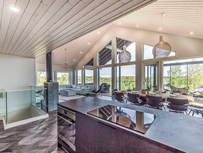 A modern kitchen with a large island, dining area with chairs, and large windows offering views. - Villa hill magia by Interhome (Kuhmoinen)