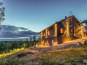 A two-story wooden house with a balcony, situated on a hillside with a view of the surrounding landscape. - Villa hill magia by Interhome (Kuhmoinen)