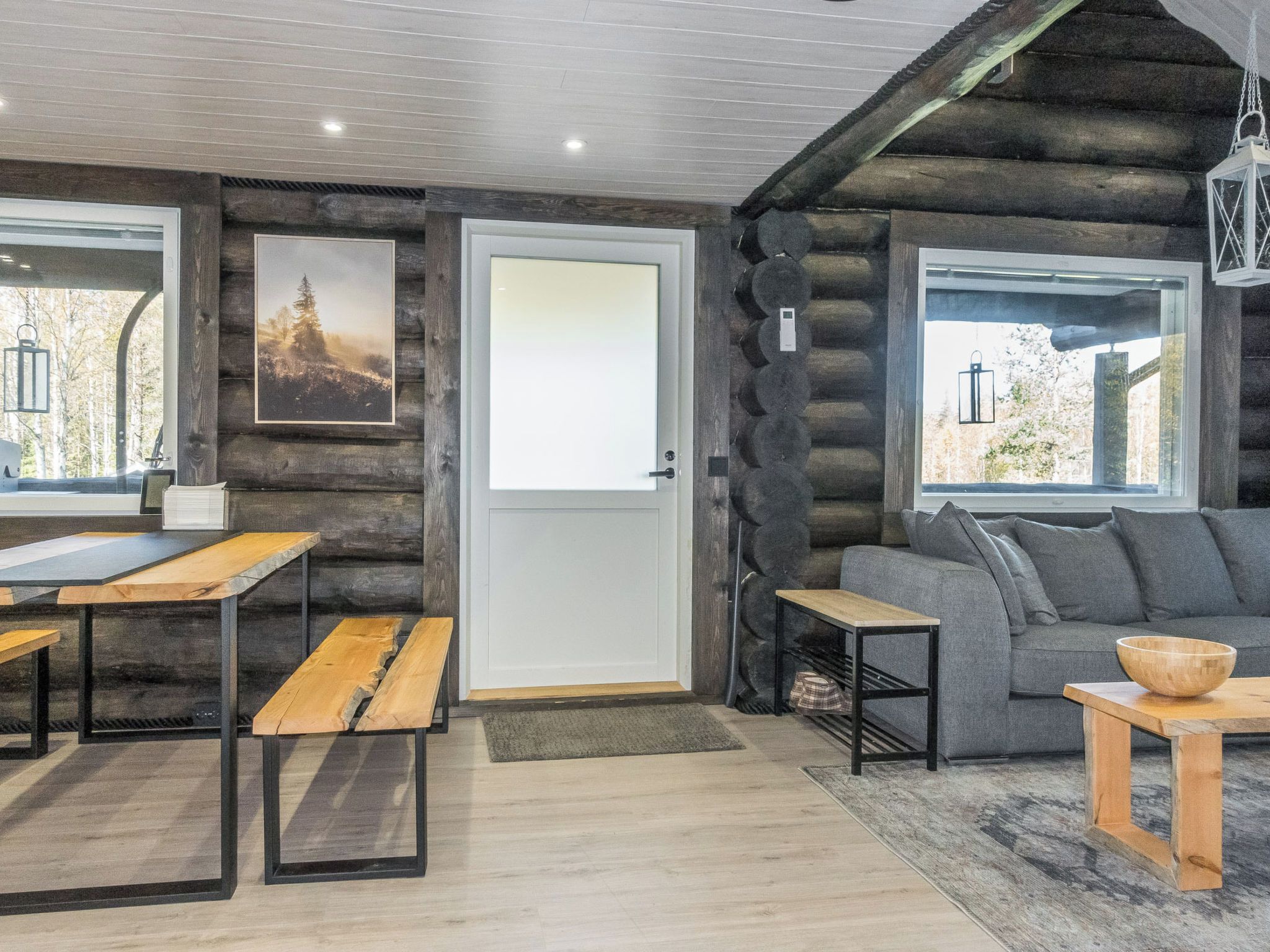 A log cabin interior with a dining area, a sofa, and a view through the windows.
