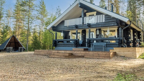 A log cabin with a porch and a small deck, surrounded by trees.