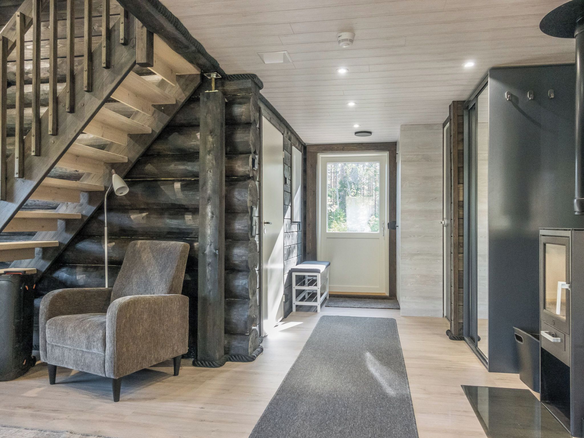 A modern interior with a wooden staircase, a grey armchair, and a door leading outside.