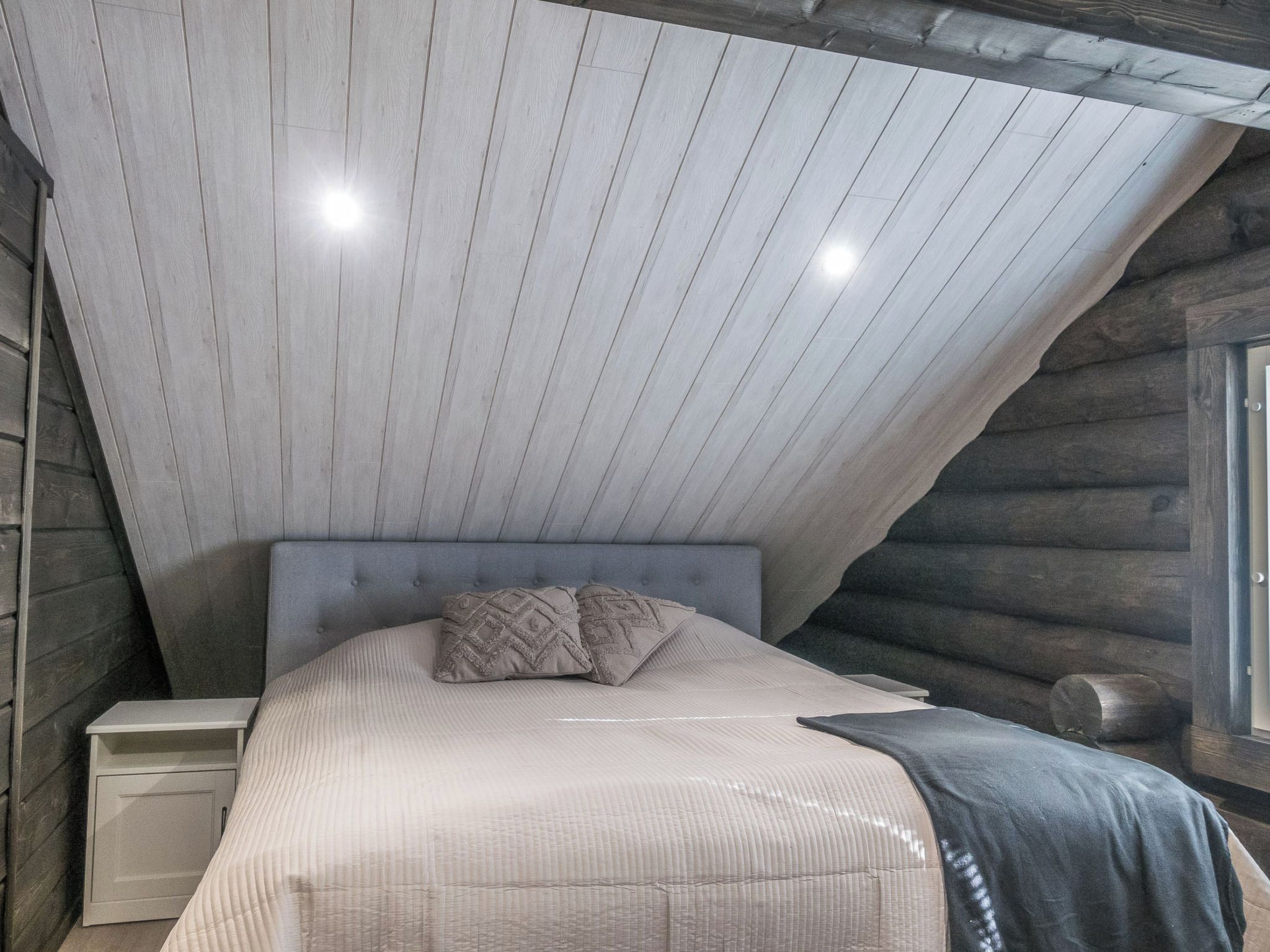 A bedroom with a sloped ceiling, a bed with a headboard, two bedside tables, and a window.
