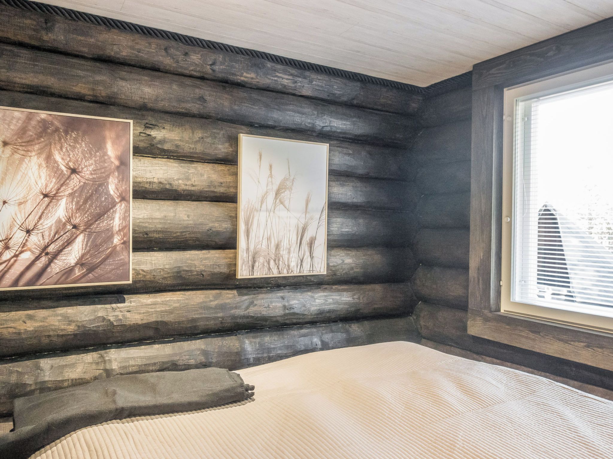 Ein Holzblockhaus-Innenraum mit einem Bett, zwei gerahmten Bildern und einem Fenster.