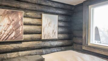 Ein Holzblockhaus-Innenraum mit einem Bett, zwei gerahmten Bildern und einem Fenster.