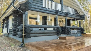 A log cabin with a wooden deck, large windows, and a balcony.
