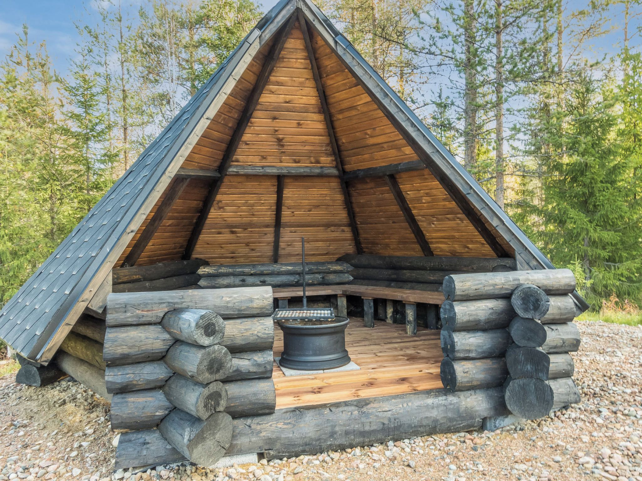 A log cabin with a triangular roof, a central hearth, and a surrounding log structure.