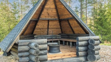 A log cabin with a triangular roof, a central hearth, and a surrounding log structure.