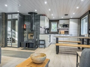 A modern kitchen with a wood-burning stove, a dining area with benches, and a large window. - Vaaranpää by Interhome (Rovaniemi)