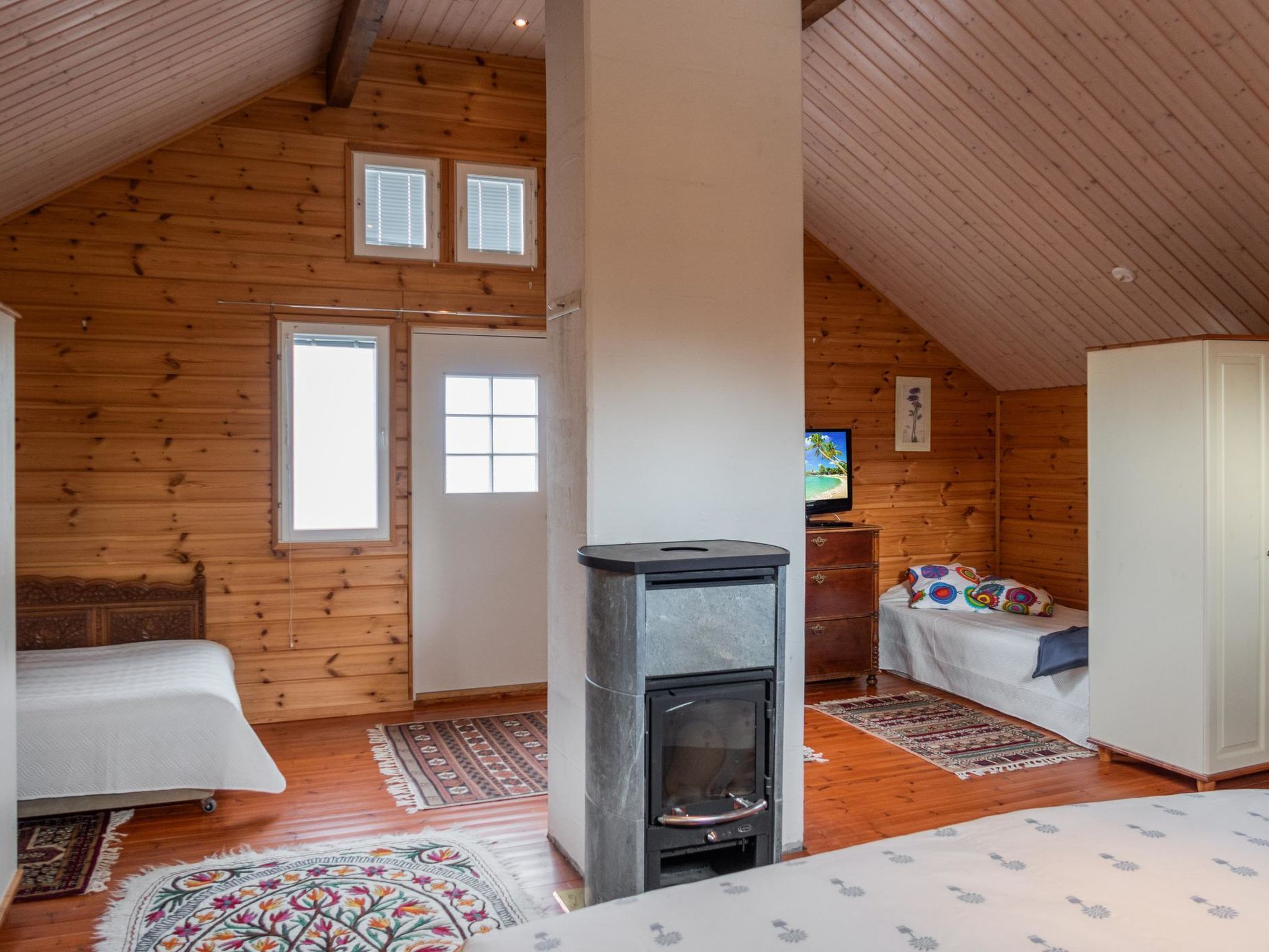 Um quarto de sótão acolhedor, com paredes de madeira, lareira, cama, televisão e guarda-roupa.