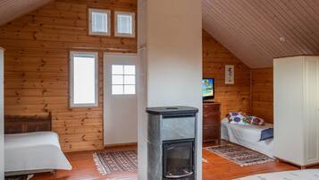 Um quarto de sótão acolhedor, com paredes de madeira, lareira, cama, televisão e guarda-roupa.