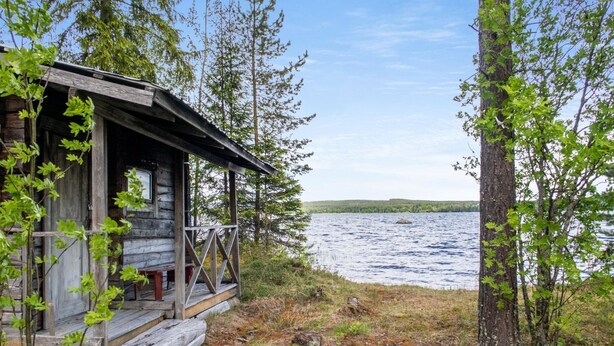 A rustic cabin with a wooden deck and a view of a lake.