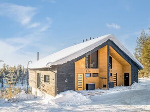 A modern log cabin with a sloped roof, large windows, and a snow-covered exterior.