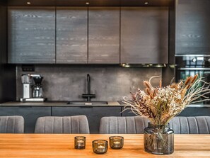 Una cocina moderna con armarios oscuros, una cafetera y un comedor con una mesa de madera y tres velas.