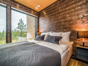 Une chambre avec un grand lit, des murs en bois, une fenêtre et une table de chevet.