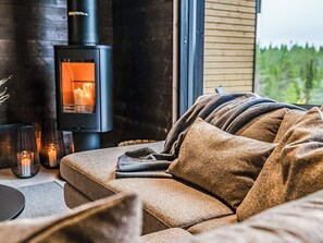En hyggelig stue med sofa, pejs og udsigt til naturen.