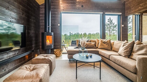 Un intérieur moderne avec un poêle à bois, un grand canapé et une vue sur l’extérieur.
