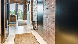 Un couloir moderne avec un lambris en bois, une porte vitrée donnant sur l’extérieur et un petit coin salon agrémenté de coussins.