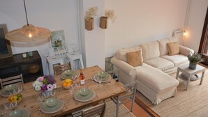 Een eetgedeelte met een houten tafel voor vier personen, omringd door stoelen. Er is een bank en een klein bijzettafeltje met een plant.