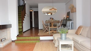 Een woonkamer met een bank, een salontafel, een open haard, een eethoek met tafel en stoelen, en een trap.
