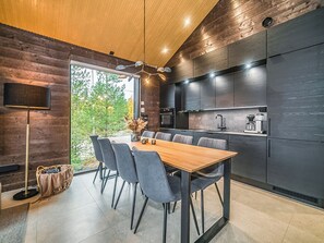 Una cocina moderna con comedor, que presenta una mesa y sillas de madera, horno empotrado y un amplio ventanal con vista a zonas verdes.