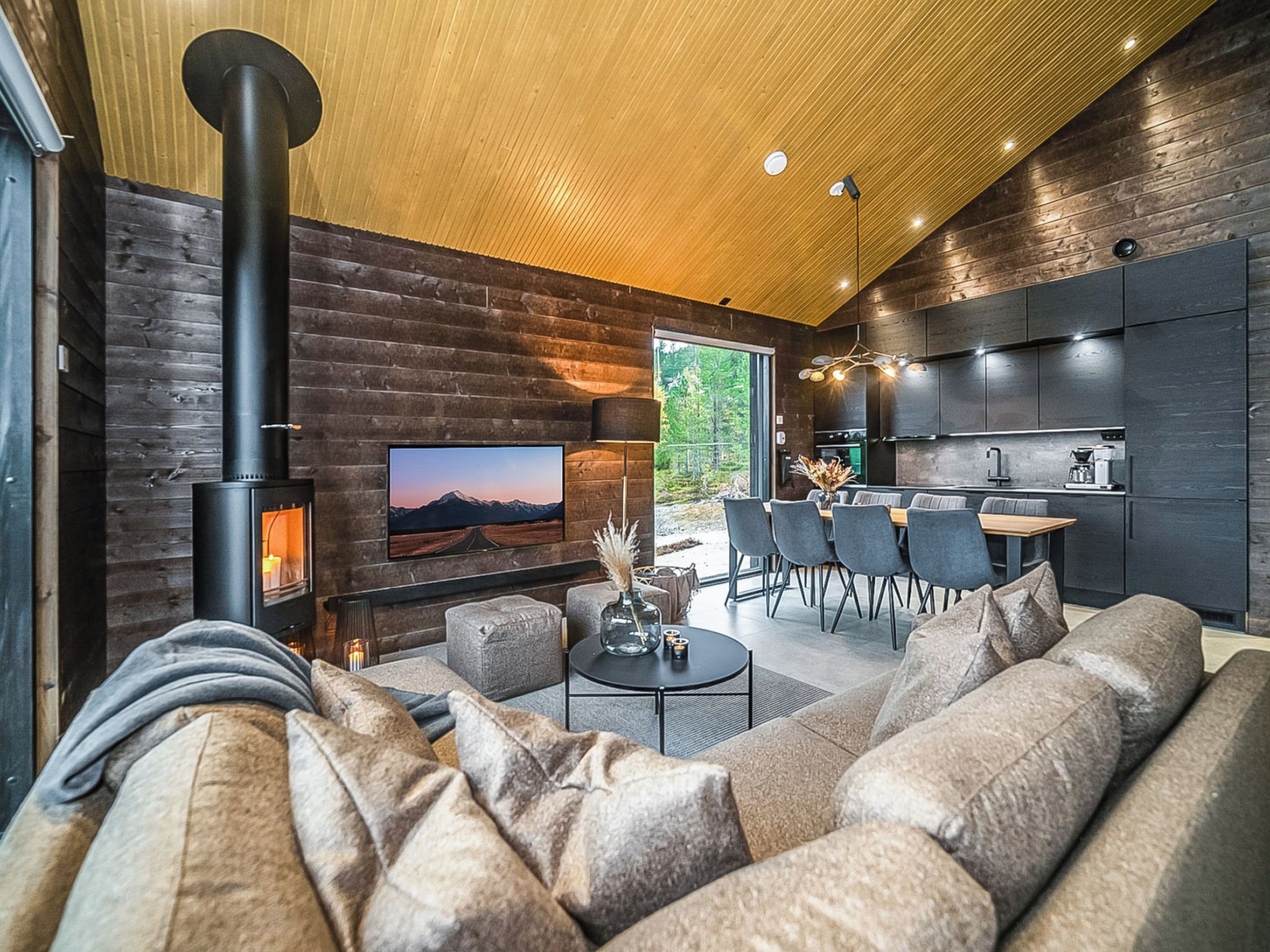 A modern living room with a large sofa, a fireplace, a television, and a dining area with chairs.