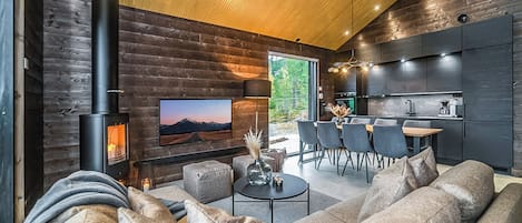 Un salon moderne avec un grand canapé, une cheminée, un téléviseur et un coin repas avec des chaises.