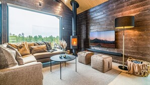 Ein gemütliches Wohnzimmer mit einer Couch, Hocker, einem Couchtisch, einem Kamin und einem großen Fenster mit schöner Aussicht.