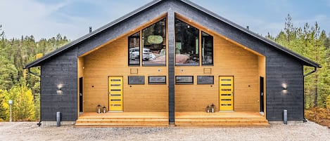 Ein modernes Blockhaus mit einer symmetrischen Fassade, großen Fenstern und einer Schotterzufahrt.