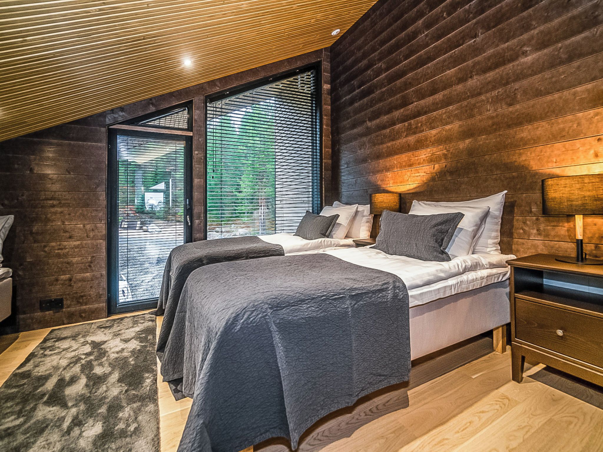 Un dormitorio con una cama grande, una mesita de noche, una lámpara y vistas al exterior a través de una ventana.