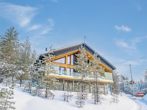 A modern two-story building with large windows and a sloped roof, surrounded by snow-covered trees and a clear sky. - Villa voimapolku 9 a 2 by Interhome (Kuusamo)