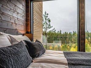 A bedroom with a large window, wooden walls, and a bed with pillows.
