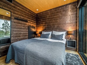 A modern bedroom with a wooden log wall, a large bed, bedside lamps, and a view of the outdoors. - Villa voimapolku 9 a 2 by Interhome (Kuusamo)