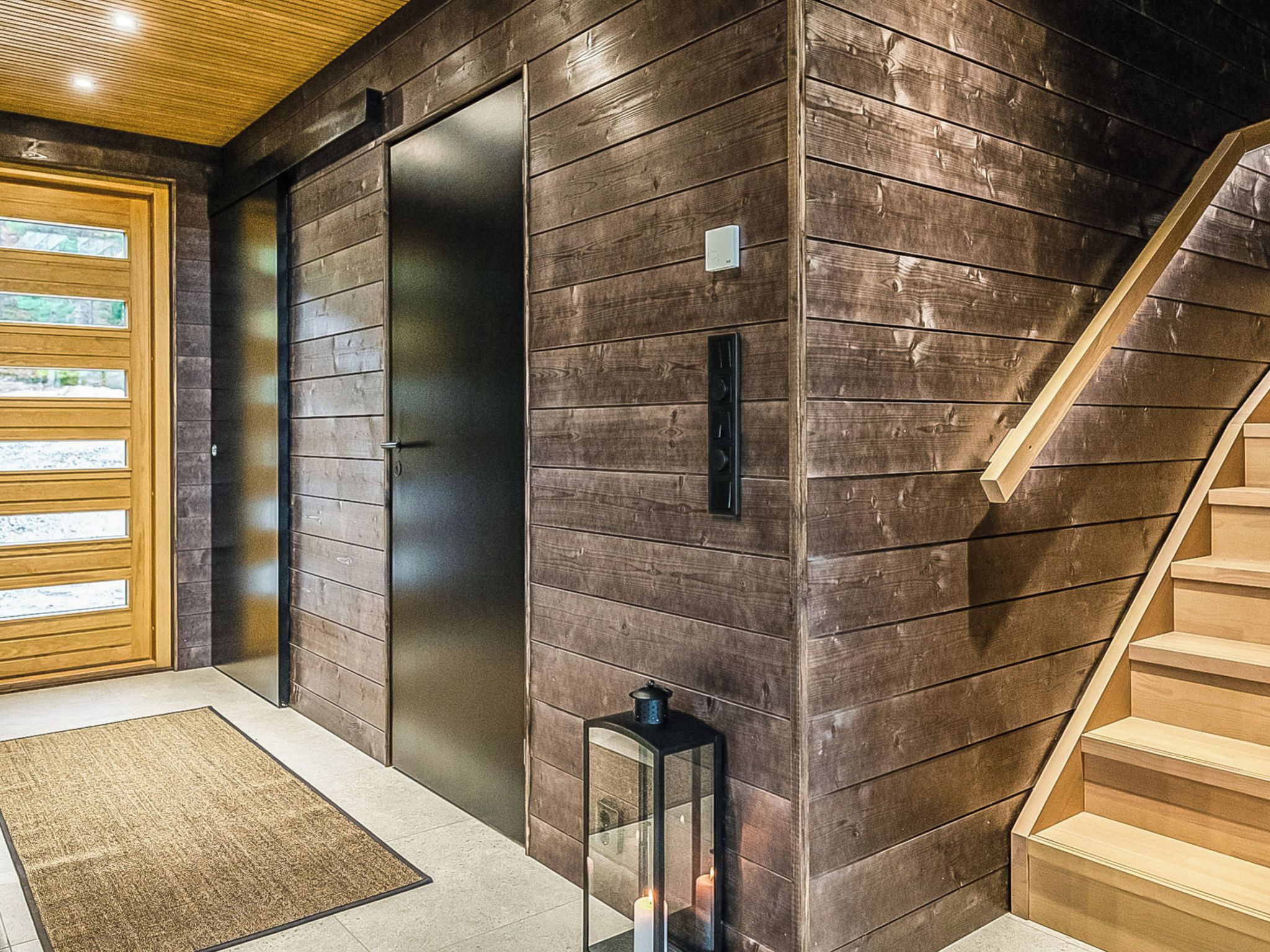 Un interno moderno con una parete in legno, una porta in vetro, una scala e un piccolo tavolo con una candela.
