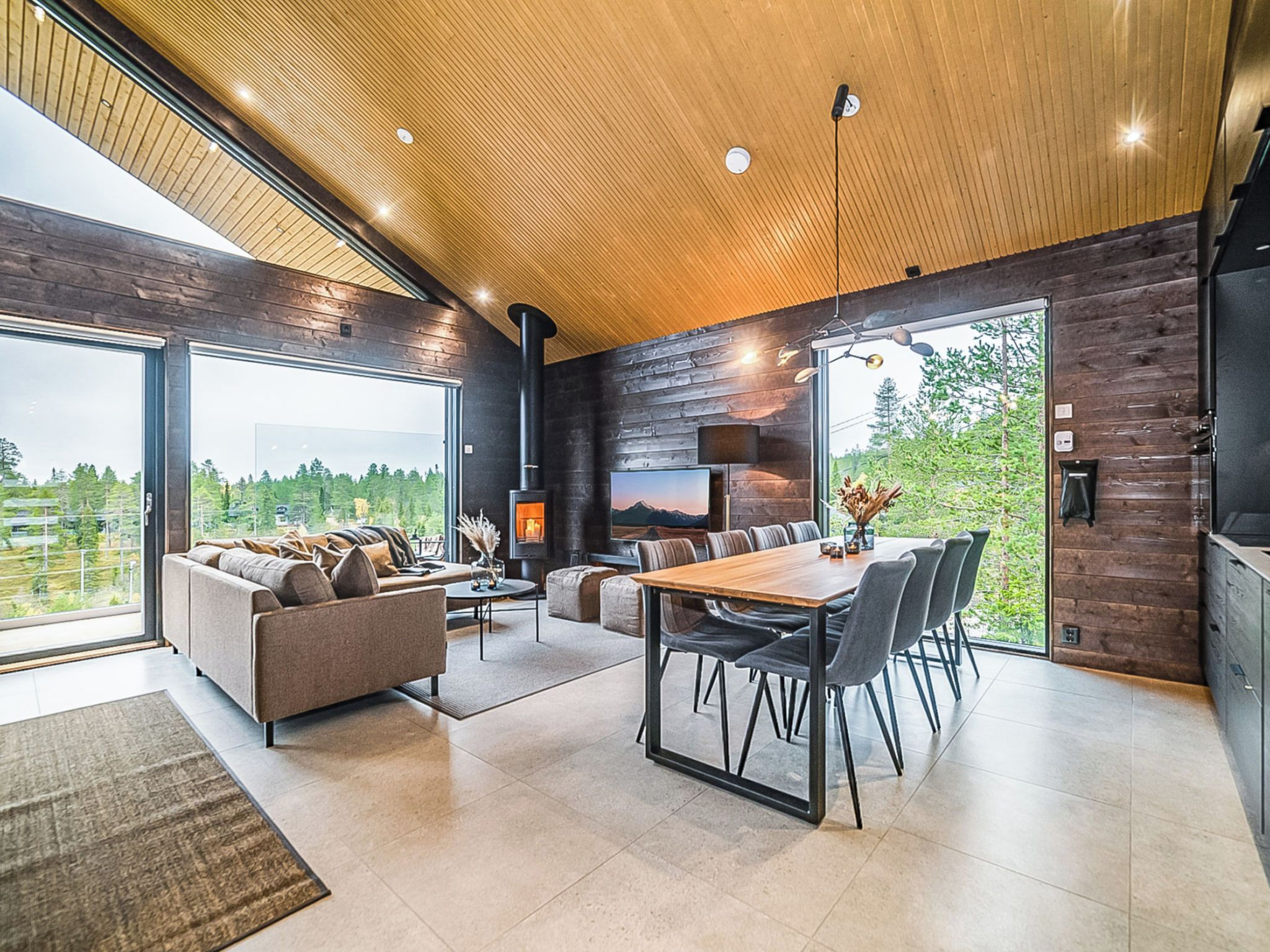 A modern interior with a dining area, sofa, and large windows offering a view of the outdoors.