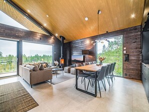 Un interior moderno con zona de comedor, sofá y ventanas amplias que ofrecen vistas al exterior.