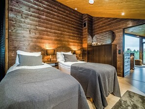 Un dormitorio de cabaña moderna con dos camas, techo de madera y un ventanal grande.