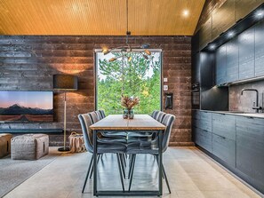 A modern kitchen with dark cabinetry, a wooden ceiling, and a dining area with a table and chairs. - Villa voimapolku 9 a 2 by Interhome (Kuusamo)
