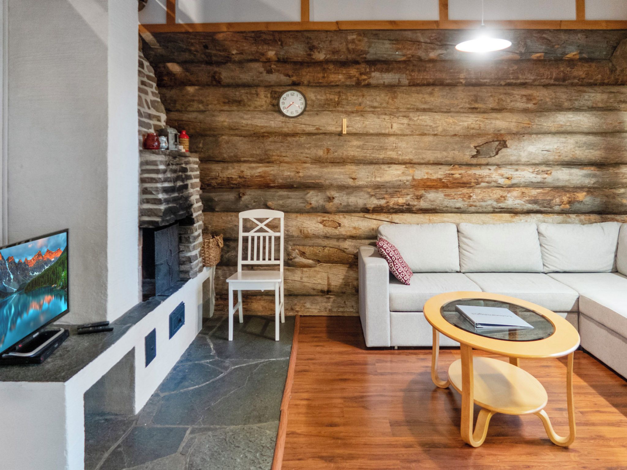 Ein gemütliches Wohnzimmer mit Kamin aus Stein, einem weißen Sofa, einem Holztisch und einem Fernseher an einer Steinsäule.