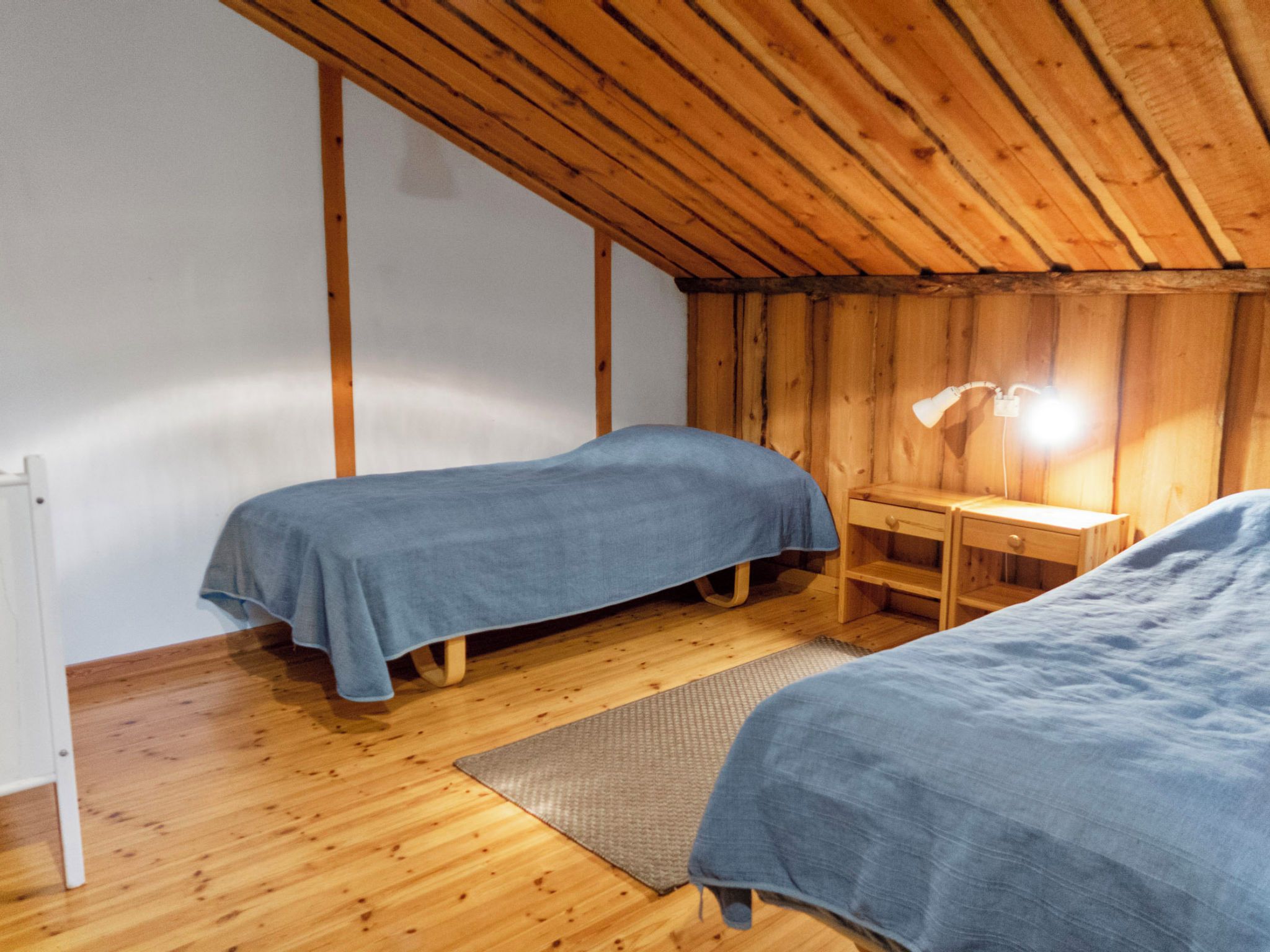 Une chambre avec deux lits, un plancher en bois, un bureau avec une lampe et un radiateur.