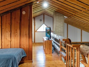 A wooden interior with a sloped ceiling, a bed, a desk with a computer, and a window with a view.