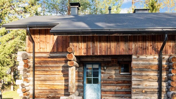 Ein rustikales Blockhaus mit blauer Tür, Schornstein und kleiner Veranda.
