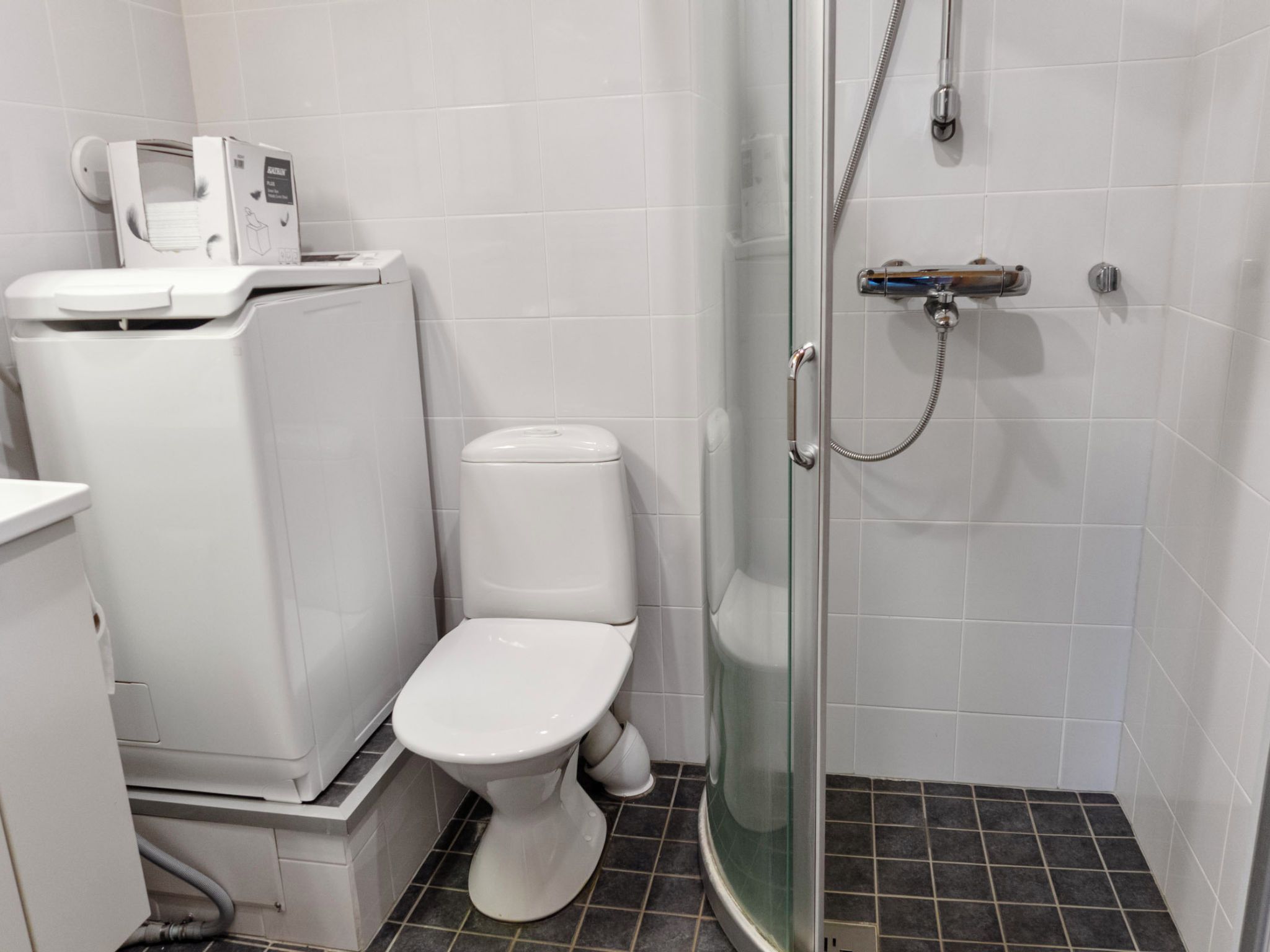 Een kleine badkamer met toilet, douche en een wasmachine.