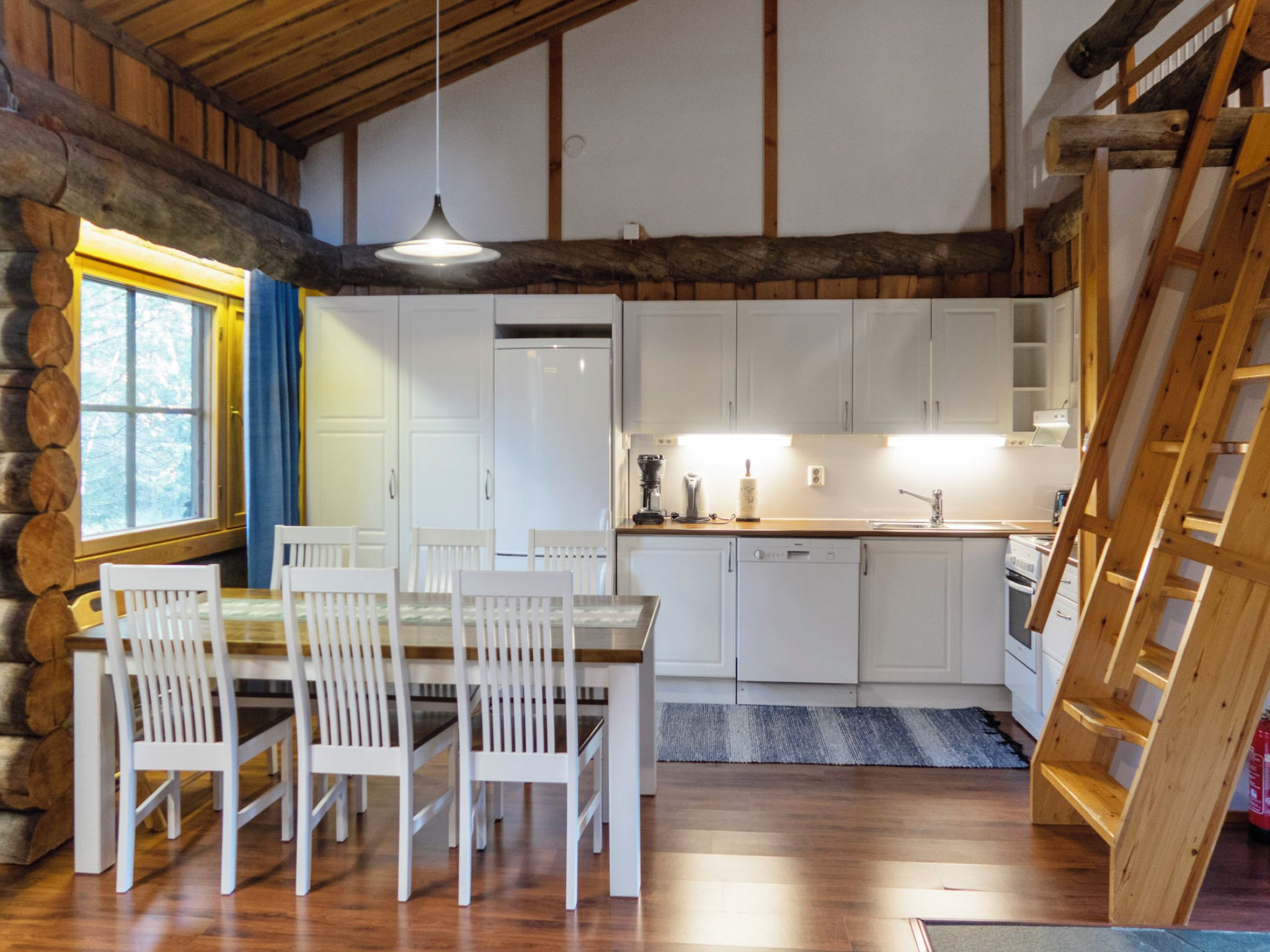 Una cocina rústica con vigas de madera, armarios blancos y una mesa de comedor con sillas.