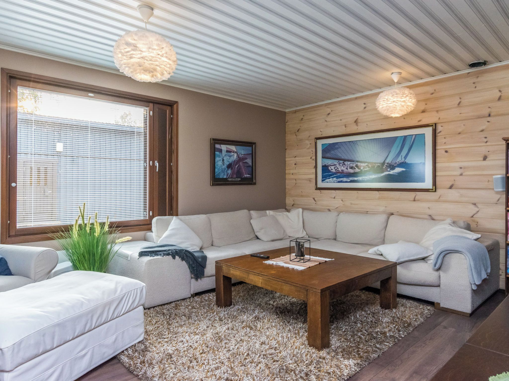 Ein modernes Wohnzimmer mit einem Ecksofa, einem Couchtisch und einem großen Fenster mit Jalousien.