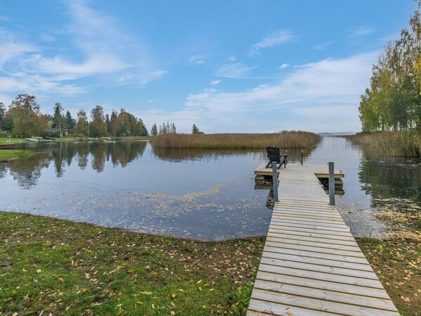 A wooden dock extending into a calm lake with a chair at the end.
