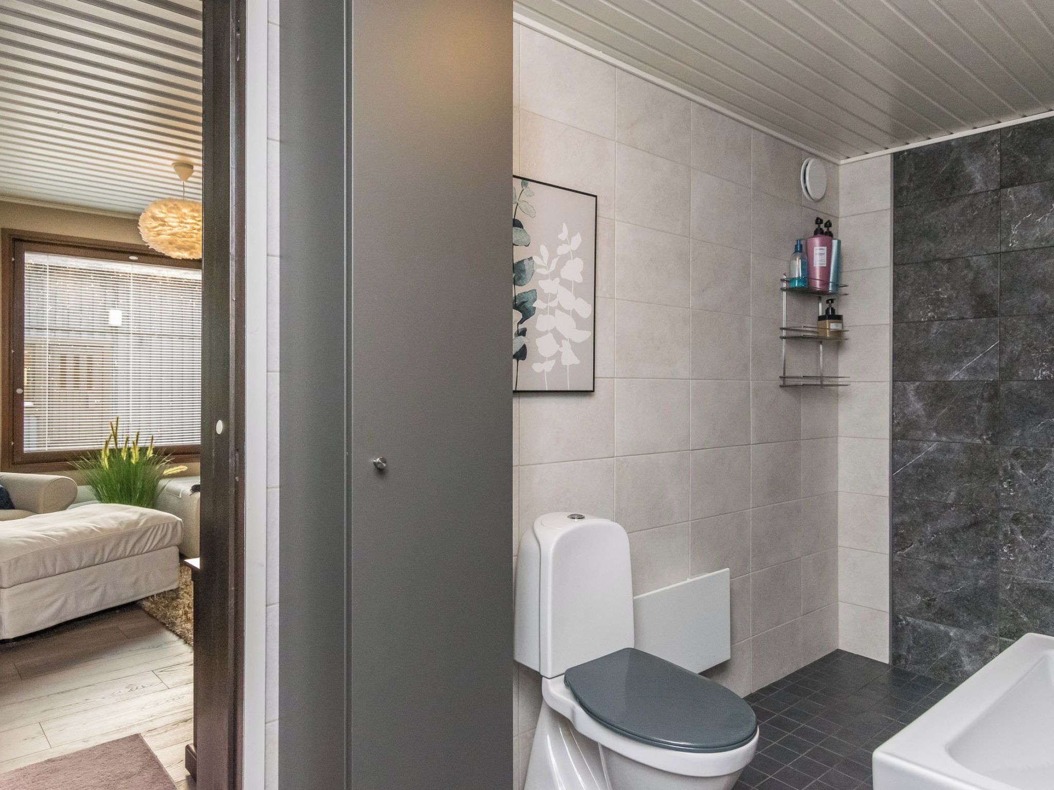 A modern bathroom with a toilet, shower, and a bathtub. There is a shelf with toiletries and a framed picture on the wall.
