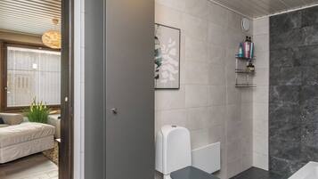 A modern bathroom with a toilet, shower, and a bathtub. There is a shelf with toiletries and a framed picture on the wall.