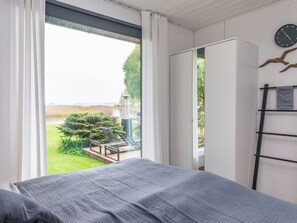 A bedroom with a bed, a wardrobe, a window with curtains, a clock, and a view of a garden. - Kiviniemi by Interhome (Kerimäki)